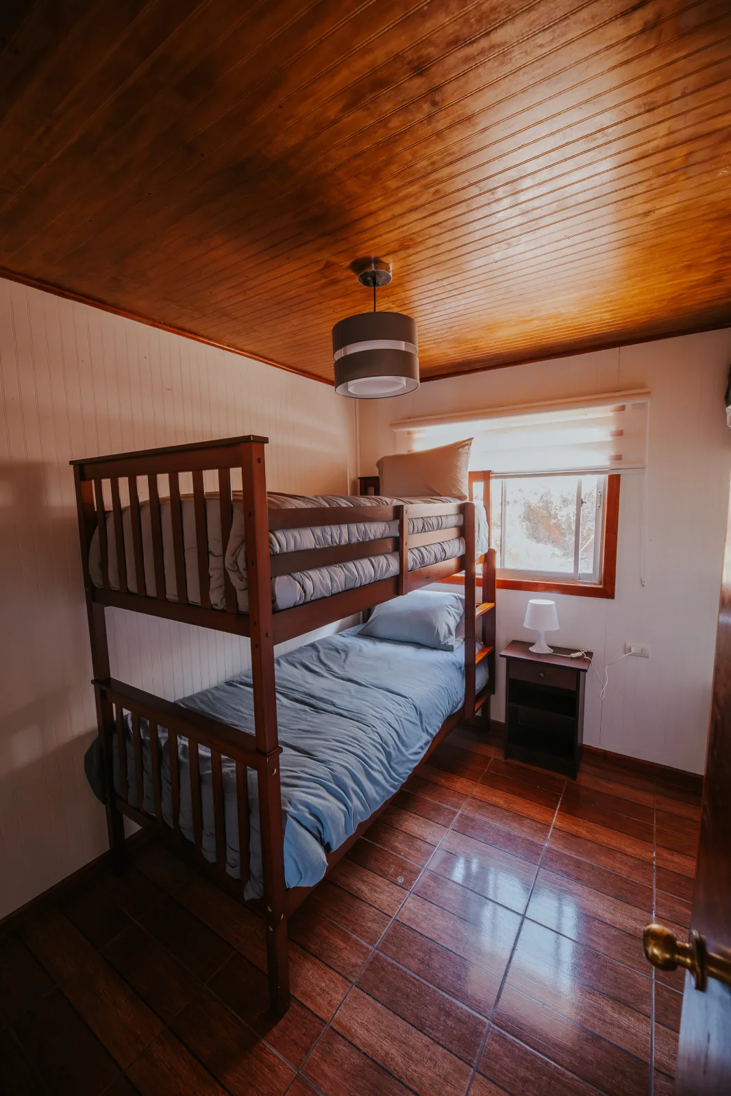 Dormitorio acogedor con litera de madera, ropa de cama gris y ventana con vista