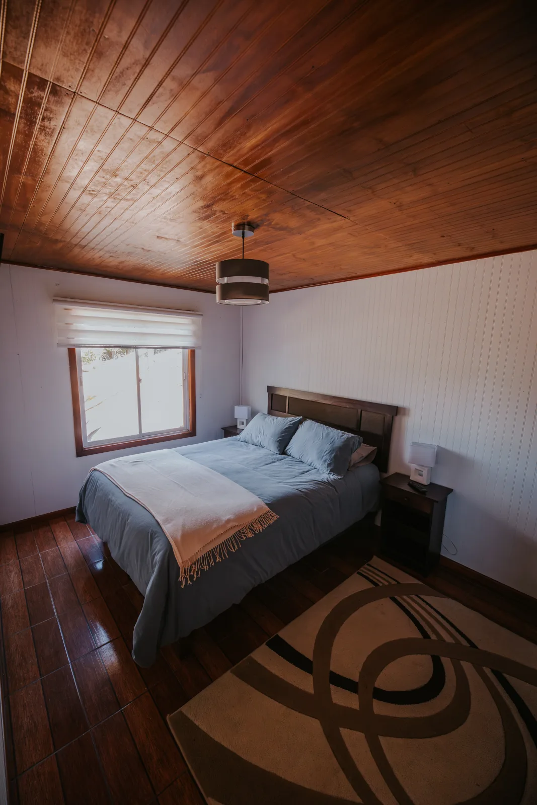 Habitación matrimonial acogedora con cama azul, techo de madera y ventana