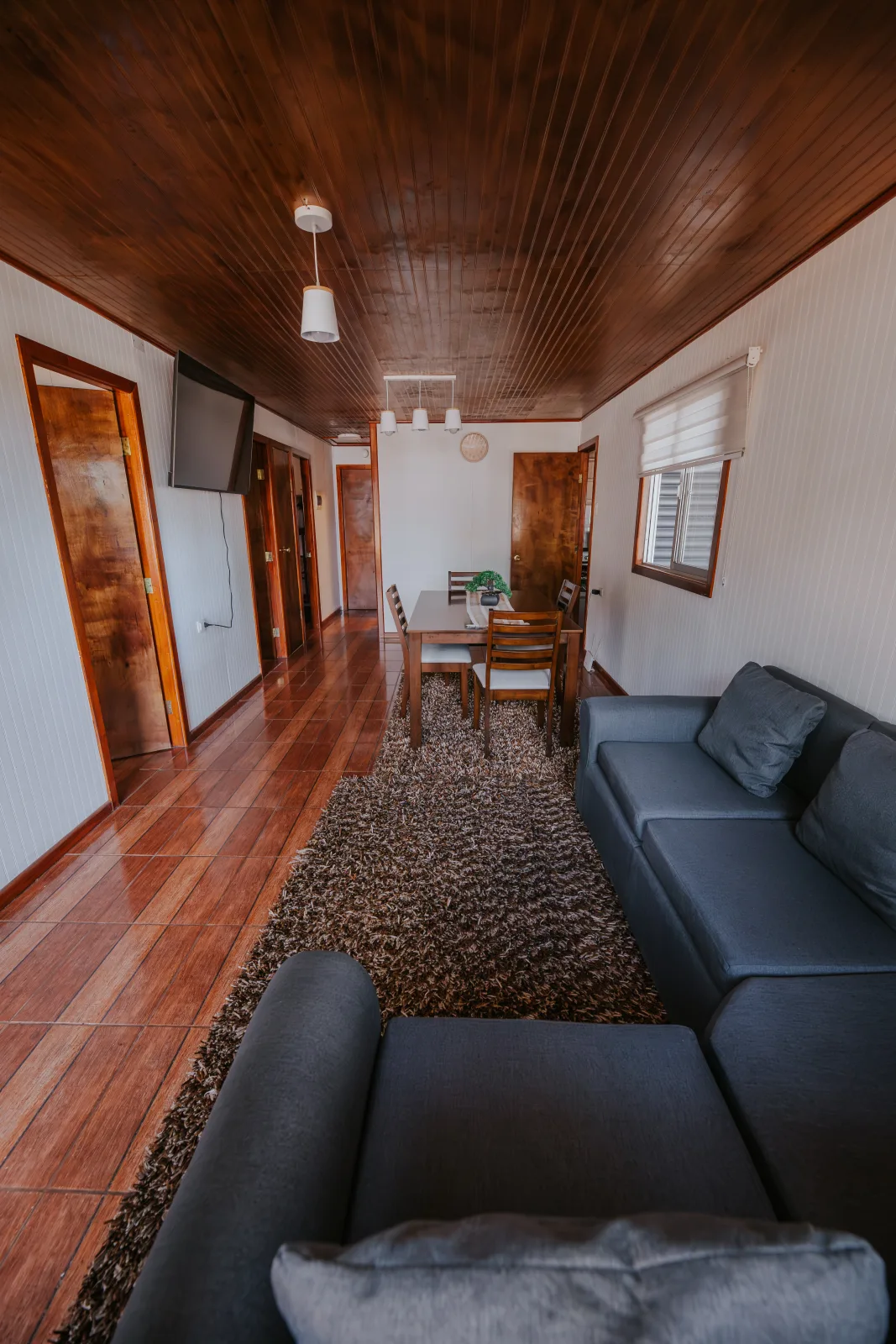 Sala de estar con dos sofás grises, comedor de madera y alfombra peluda