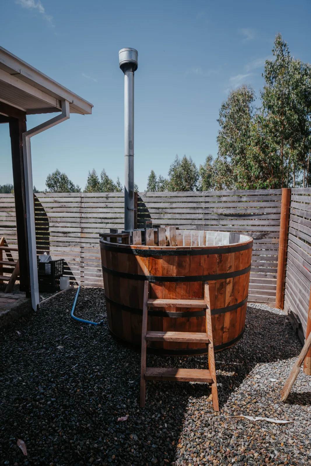 Tinaja de madera con chimenea en patio exterior soleado rodeado de cerco y árboles