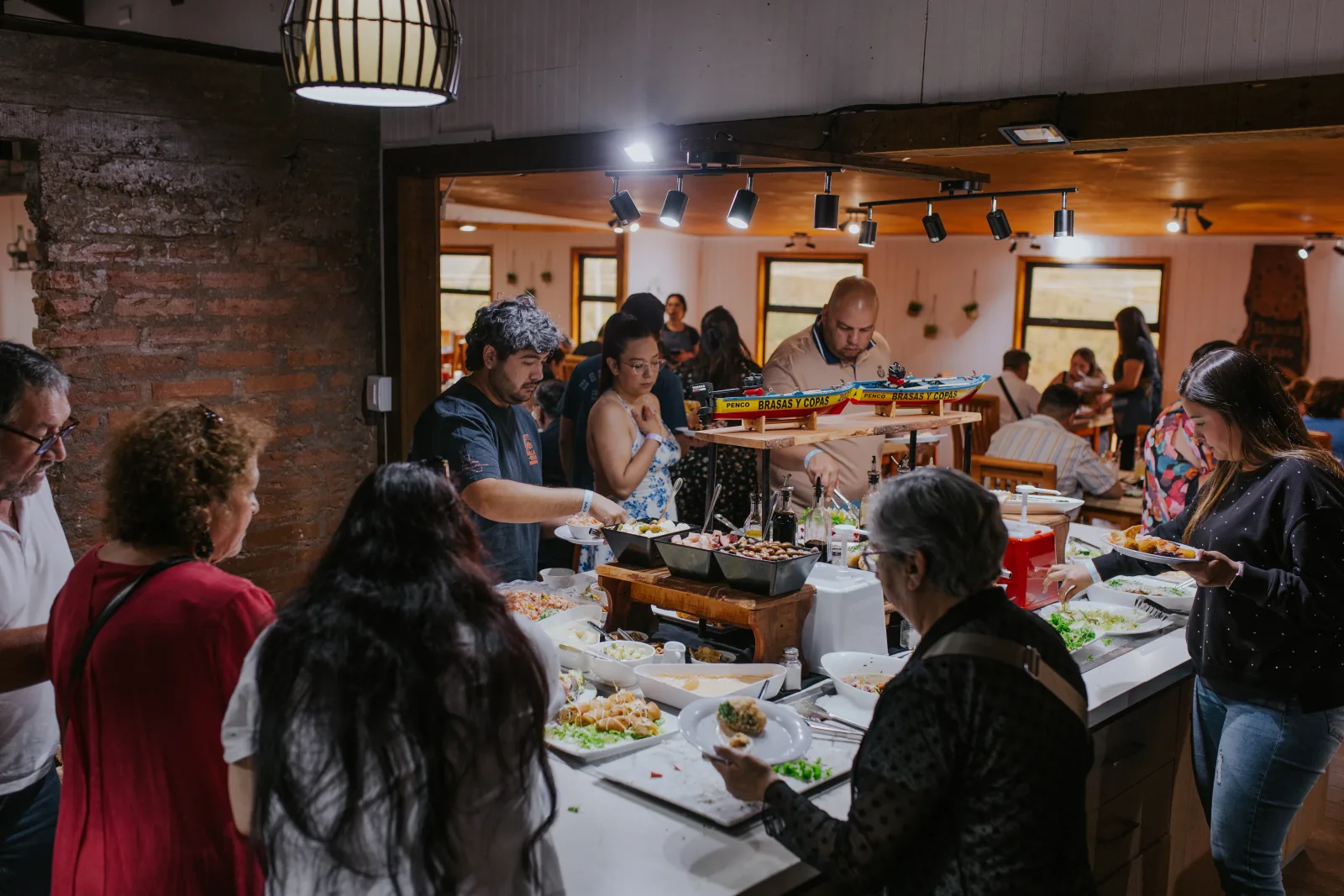 Grupo de comensales sirviéndose platos en el buffet del restaurante con iluminación cálida
