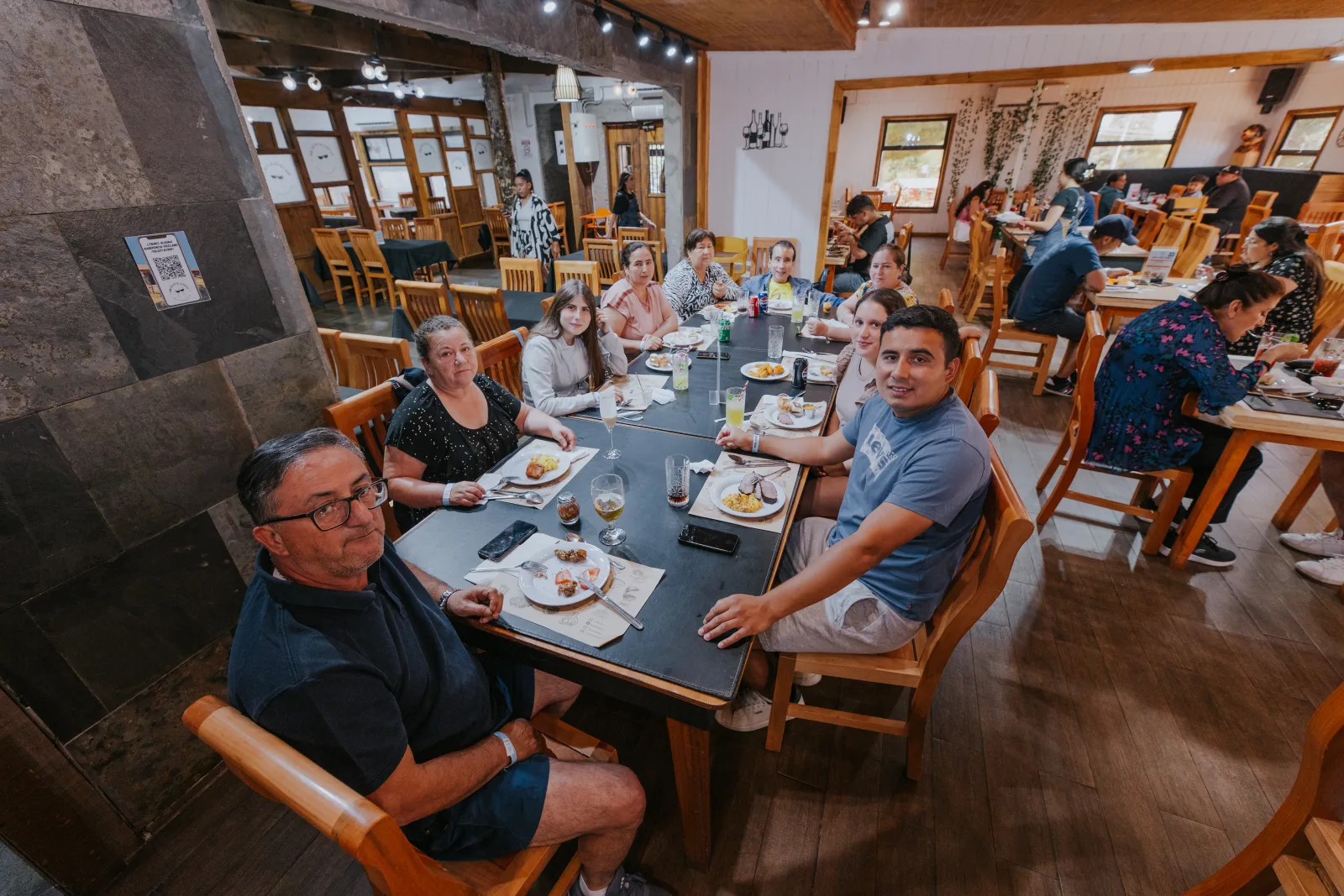 Familia numerosa sonriente compartiendo almuerzo en mesa larga