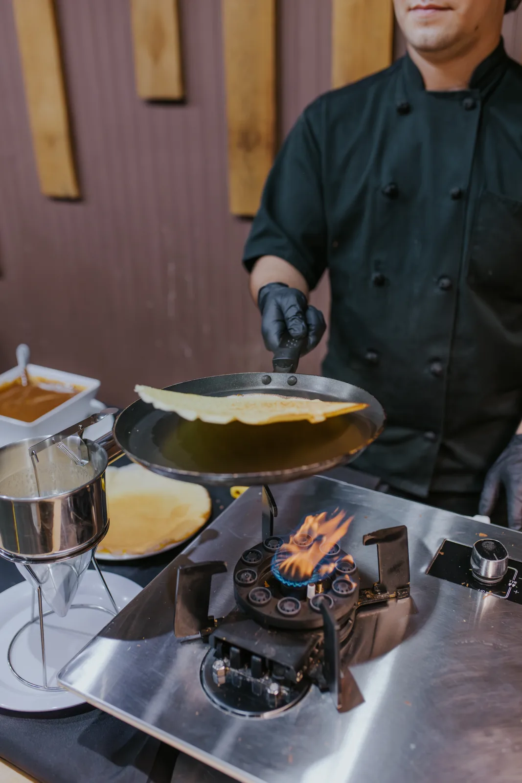 Cocinero preparando crepes en sartén sobre quemador con llama en una estación de cocina en vivo