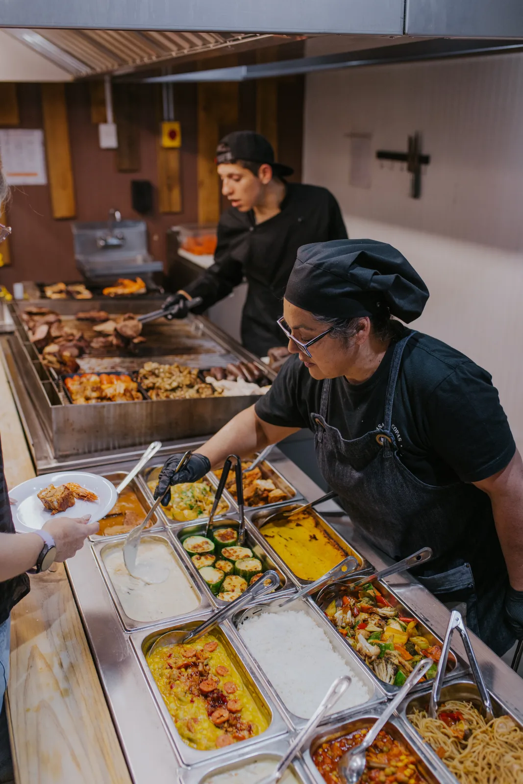 Equipo de cocina con delantal negro sirviendo guarniciones calientes en el buffet