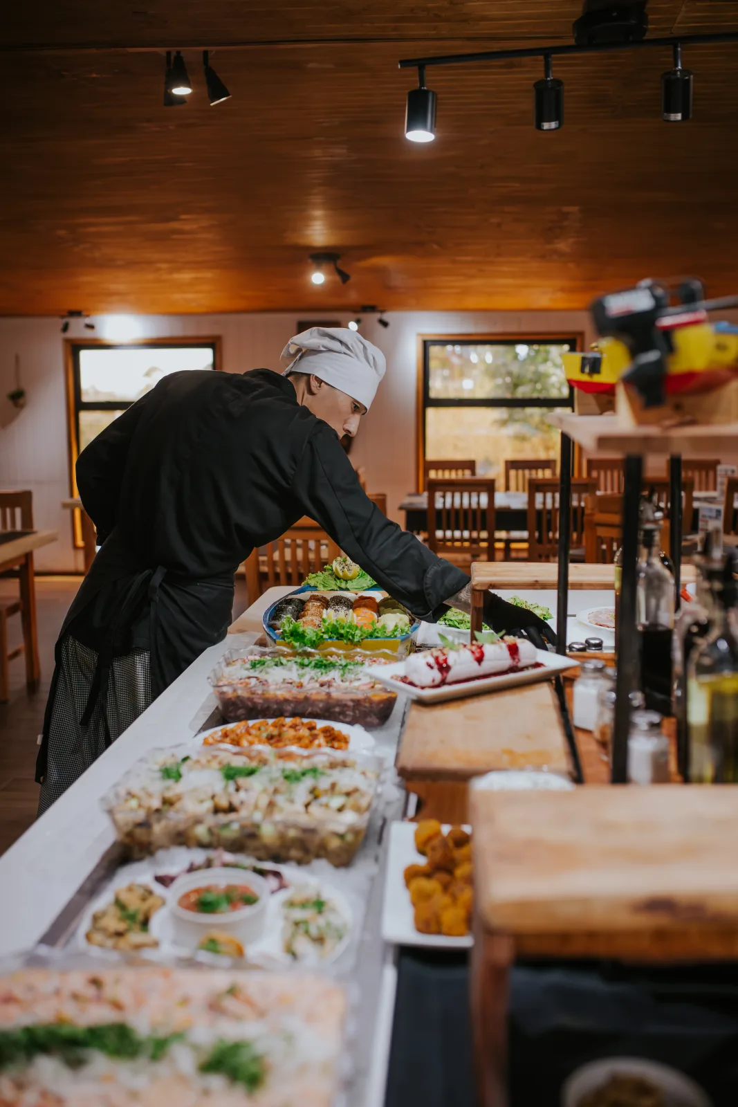 Cocinero con gorro arregla bandejas de sushi y ensaladas en el buffet del restaurante de madera