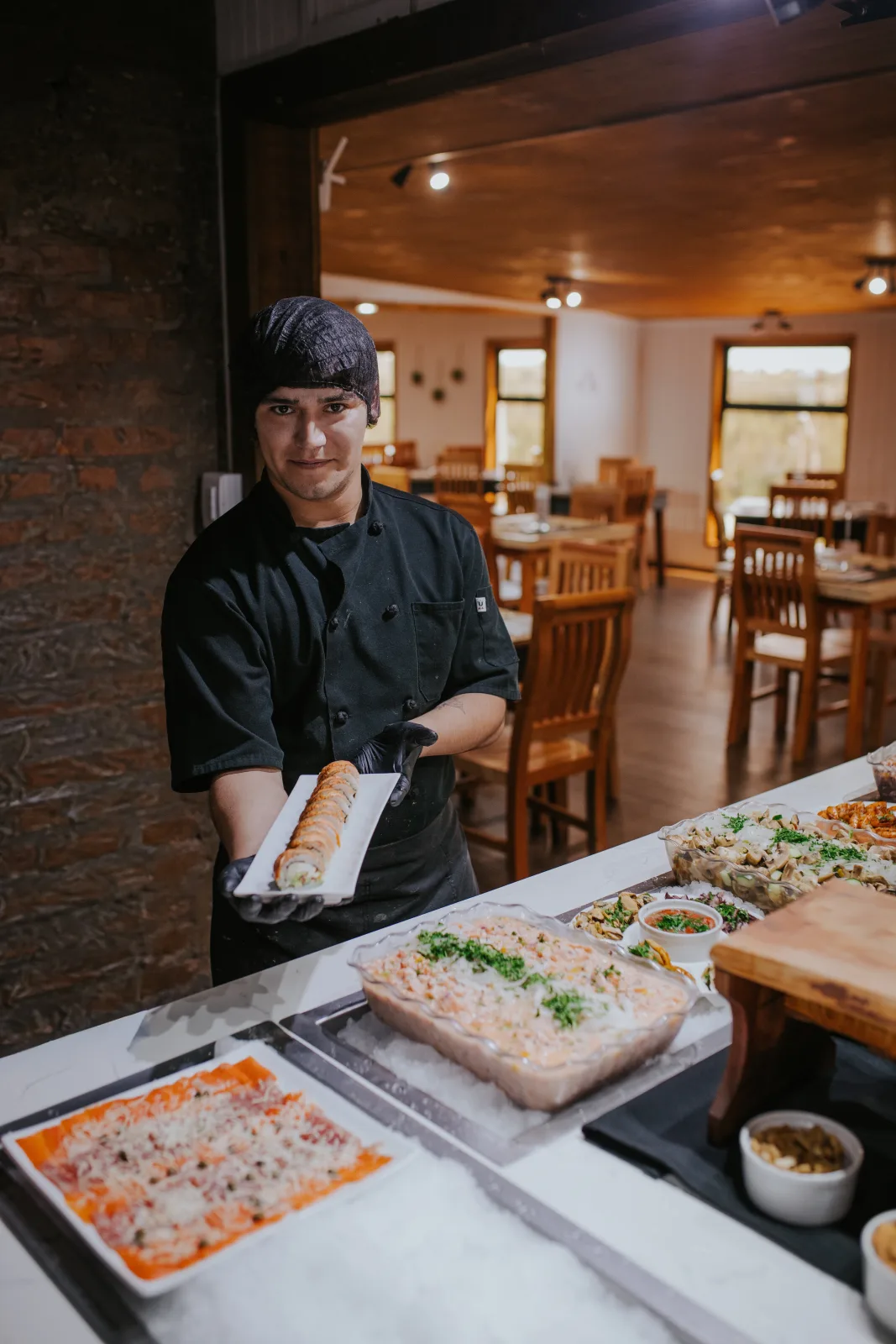 Cocinero del restaurante sostiene plato de sushi junto a barra fría con mariscos
