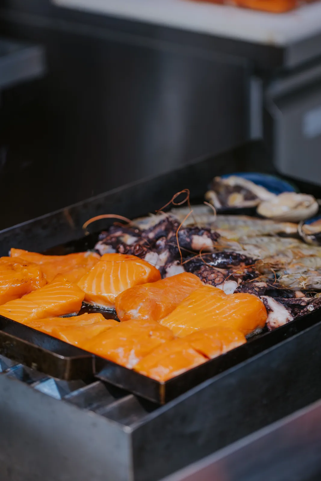 Plancha caliente con salmón, pulpo, camarones y machas frescas cocinándose en la parrilla de mariscos