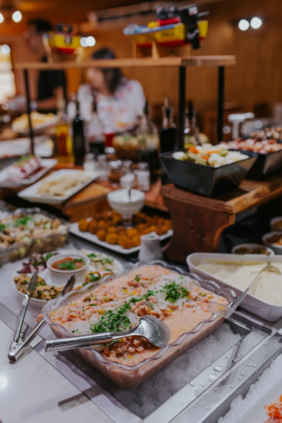 Barra fría con ceviche de salmón, croquetas y ensaladas variadas mientras comensales se sirven al fondo