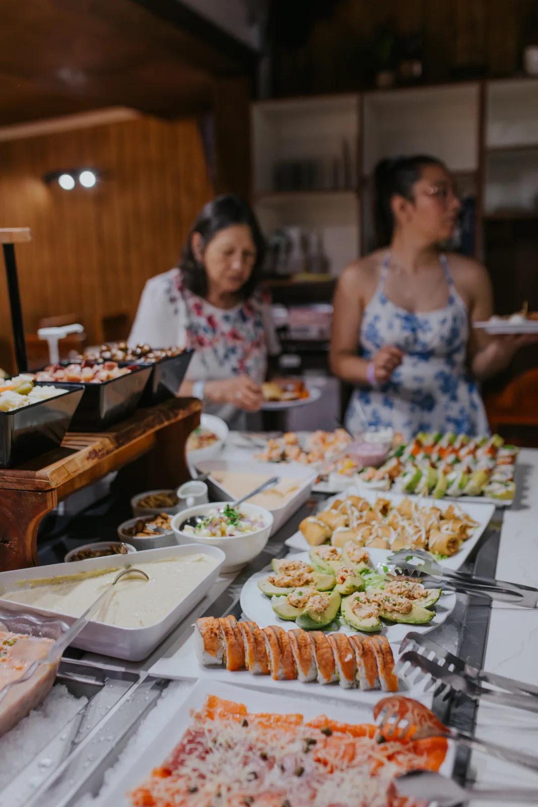Mesa buffet con sushi, ceviches y paltas rellenas mientras dos comensales se sirven en el restaurante