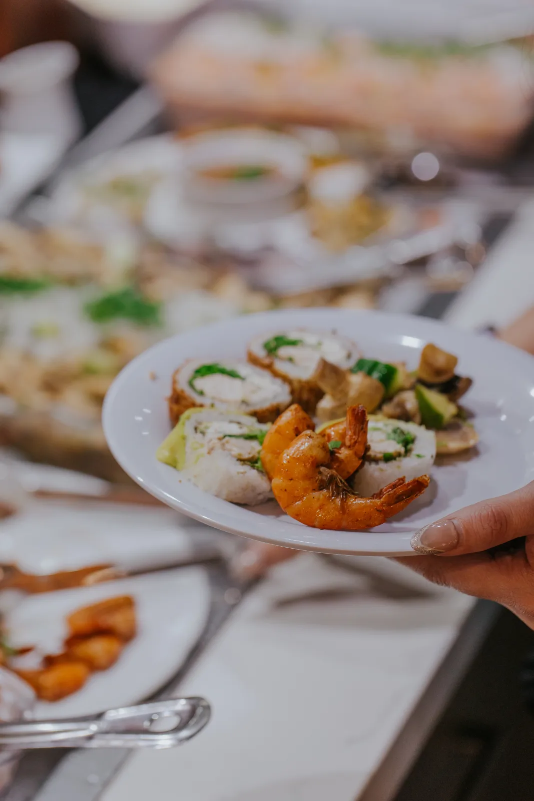 Plato servido con rolls de sushi, camarones dorados y verduras salteadas en el buffet