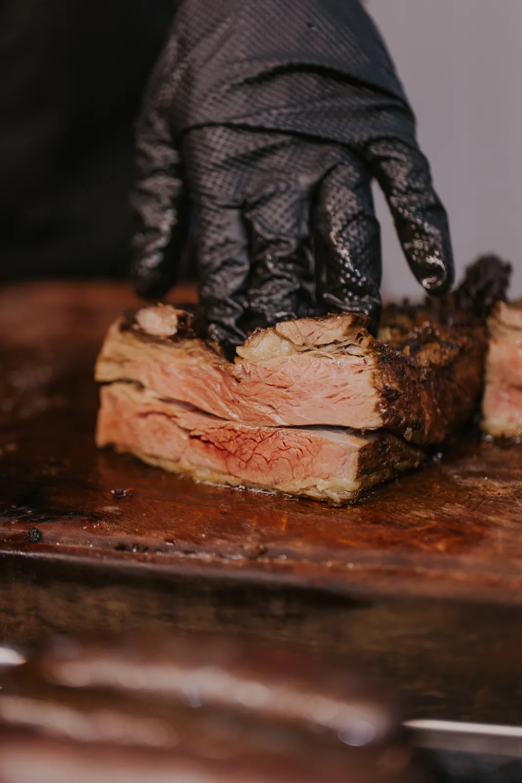 Mano enguantada sostiene corte de carne asada jugosa y sangrante sobre tabla de madera