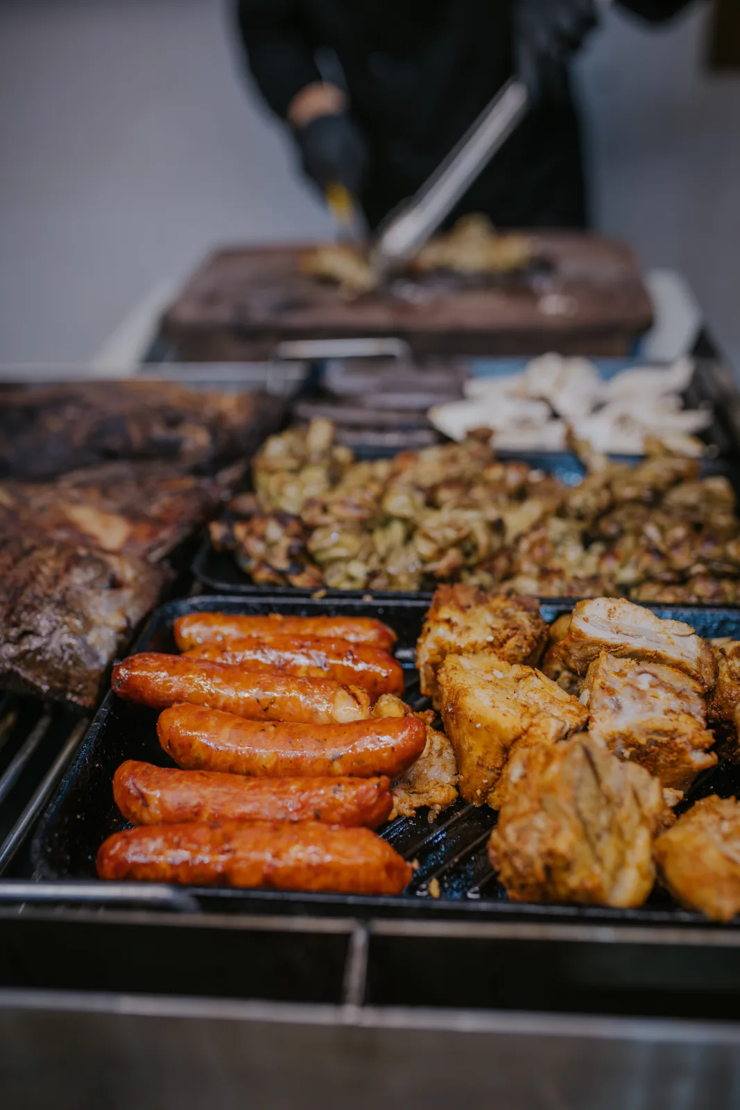 Parrillero sirviendo longanizas, costillar de cerdo y verduras grilladas en bandejas
