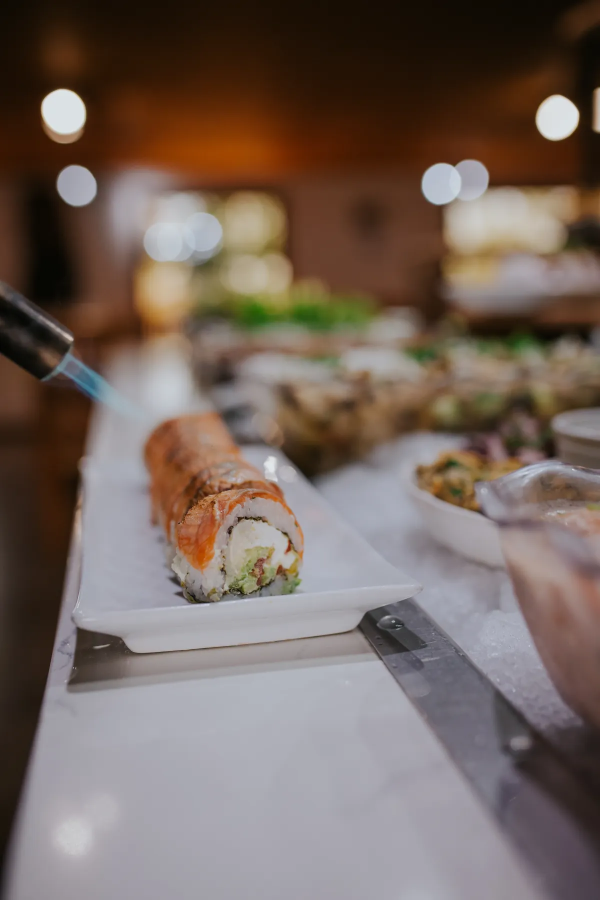 Soplete flameando un roll de sushi de salmón en la barra fría
